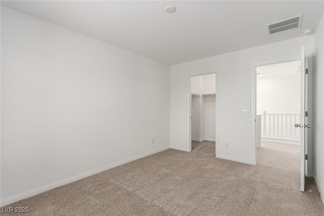 unfurnished bedroom with light colored carpet and a walk in closet