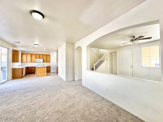 unfurnished living room with ceiling fan, light carpet, and a textured ceiling