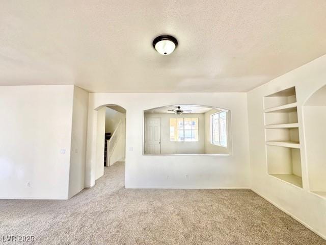 carpeted spare room featuring built in shelves and a textured ceiling