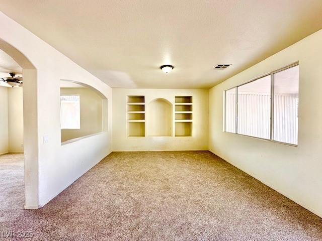 unfurnished room with built in shelves, ceiling fan, and carpet flooring