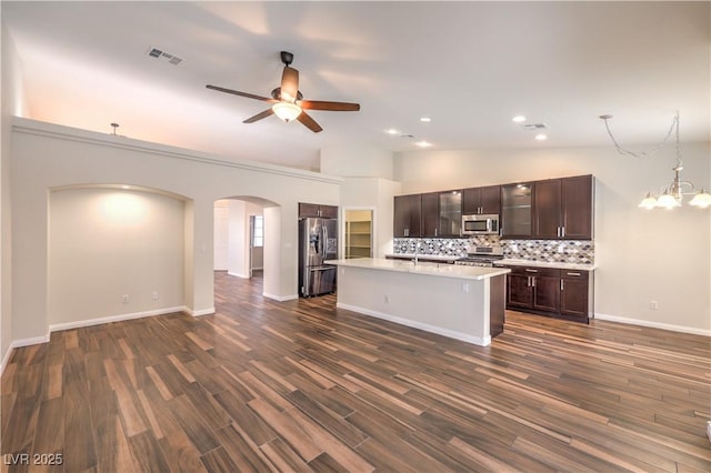 kitchen featuring appliances with stainless steel finishes, pendant lighting, decorative backsplash, a kitchen island with sink, and dark brown cabinets