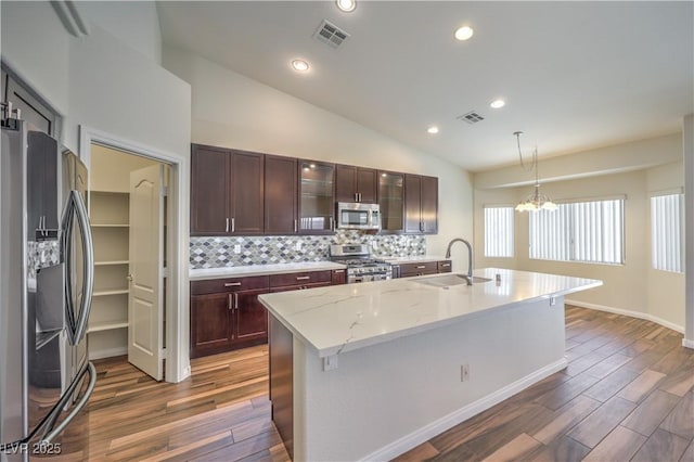 kitchen with vaulted ceiling, pendant lighting, sink, a kitchen island with sink, and stainless steel appliances