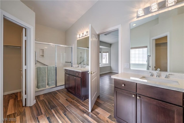 bathroom featuring a walk in closet, two vanities, a stall shower, a sink, and wood finished floors