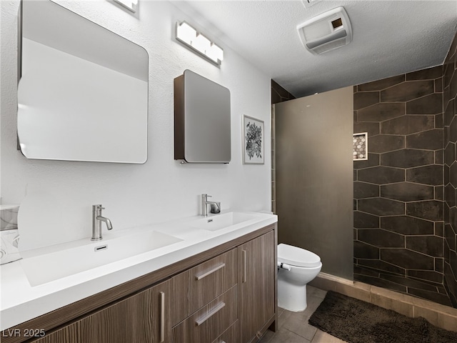 bathroom featuring tiled shower, toilet, a textured ceiling, vanity, and tile patterned flooring