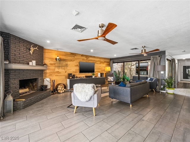 living room featuring ceiling fan, a textured ceiling, a brick fireplace, and wood walls