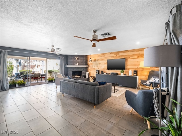 living room with a textured ceiling, light tile patterned floors, wooden walls, ceiling fan, and a fireplace