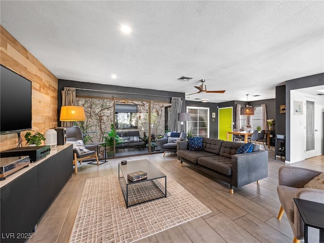 living room with ceiling fan, a healthy amount of sunlight, a textured ceiling, and wood walls