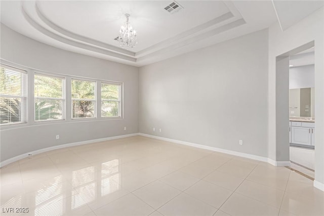 tiled spare room featuring a raised ceiling and a notable chandelier