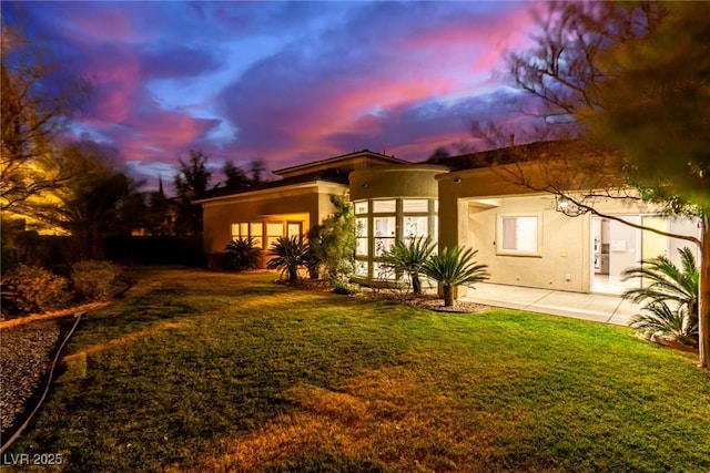 back house at dusk featuring a lawn