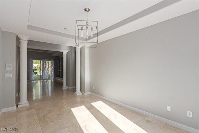 unfurnished room featuring decorative columns, a notable chandelier, and a tray ceiling