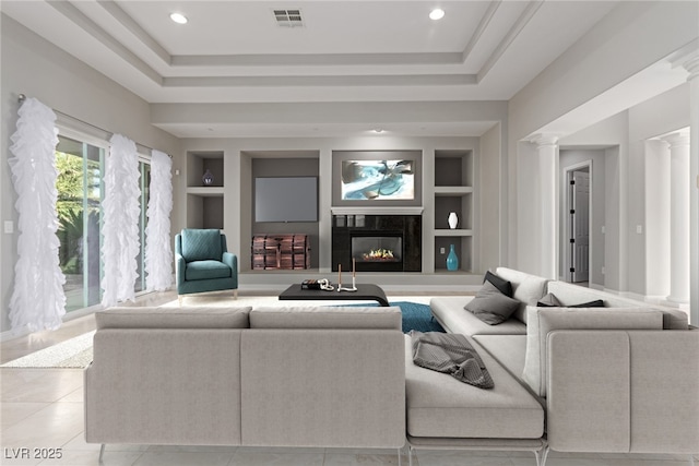 tiled living room featuring built in shelves, a high end fireplace, a tray ceiling, and ornate columns