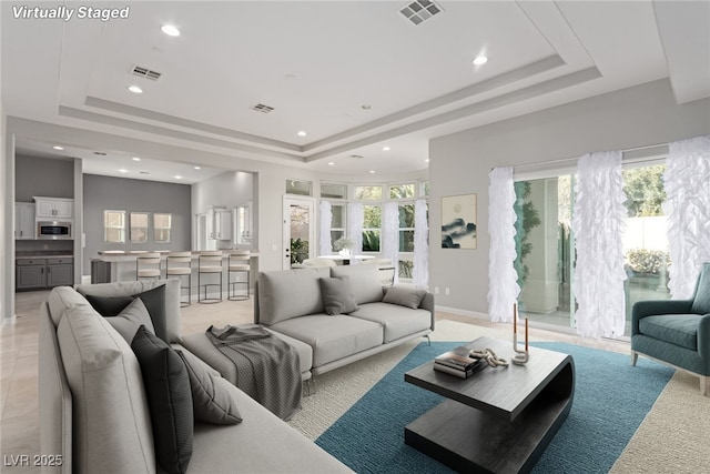 living area featuring a tray ceiling, visible vents, and recessed lighting