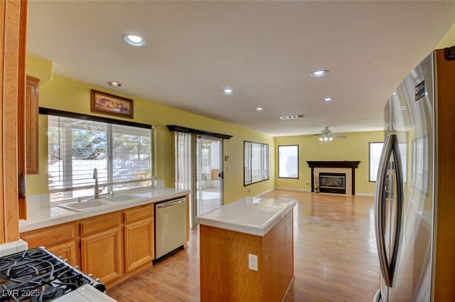 kitchen with sink, tile countertops, light hardwood / wood-style flooring, appliances with stainless steel finishes, and a kitchen island