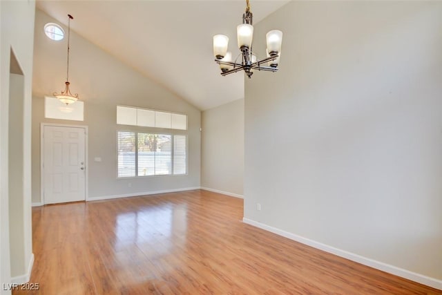 empty room with a chandelier, high vaulted ceiling, light wood-type flooring, and baseboards