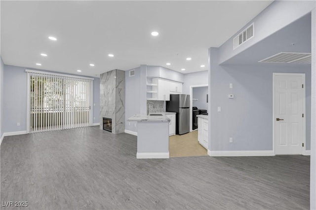 kitchen featuring a fireplace, sink, stainless steel fridge, white cabinets, and light wood-type flooring