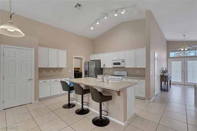 kitchen featuring a center island with sink, white cabinetry, pendant lighting, and white appliances