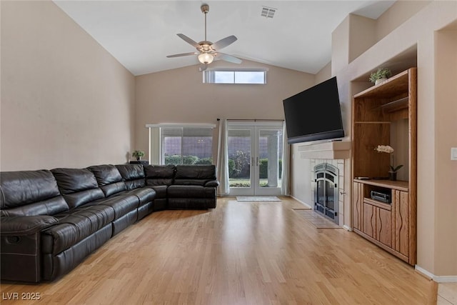 living room featuring a tile fireplace, a wealth of natural light, ceiling fan, and light hardwood / wood-style flooring