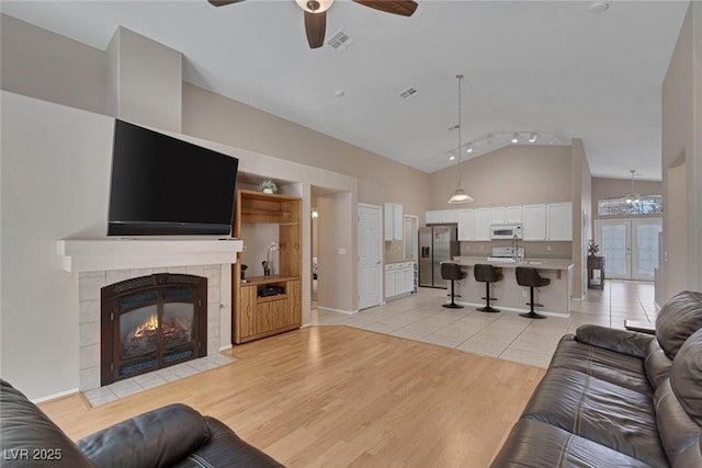 living room featuring a tile fireplace, high vaulted ceiling, ceiling fan, track lighting, and light hardwood / wood-style flooring