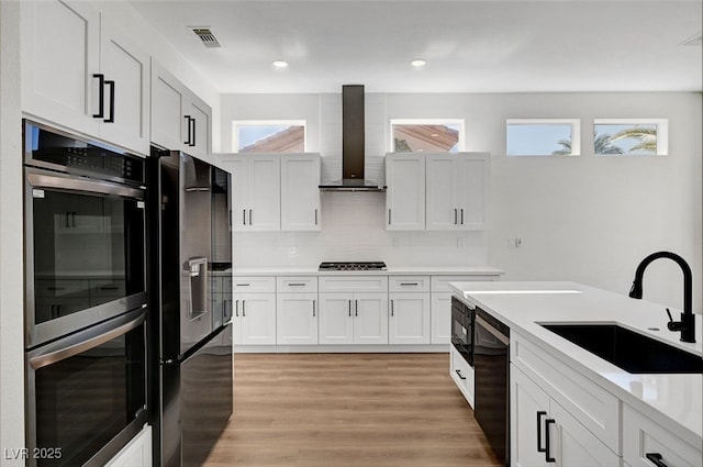 kitchen with stainless steel appliances, white cabinetry, sink, and wall chimney range hood