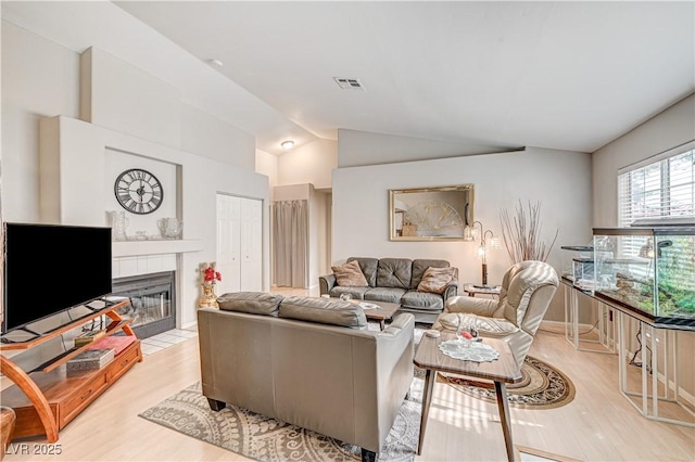 living room with vaulted ceiling, a tile fireplace, and light wood-type flooring