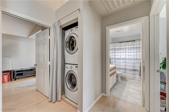 laundry area featuring stacked washer and clothes dryer and light wood-type flooring