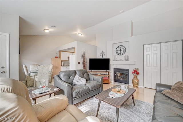 living room with lofted ceiling, a tiled fireplace, and light hardwood / wood-style floors