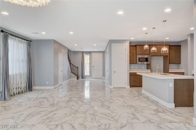 kitchen featuring stainless steel microwave, sink, a kitchen island with sink, and hanging light fixtures