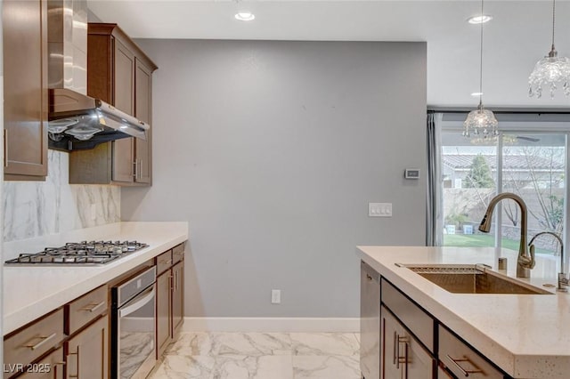 kitchen with decorative light fixtures, sink, backsplash, stainless steel appliances, and wall chimney range hood