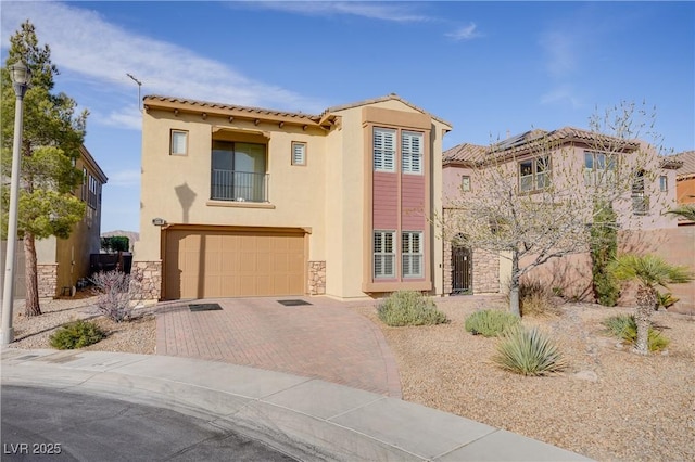 mediterranean / spanish-style house featuring decorative driveway, stucco siding, an attached garage, a balcony, and stone siding