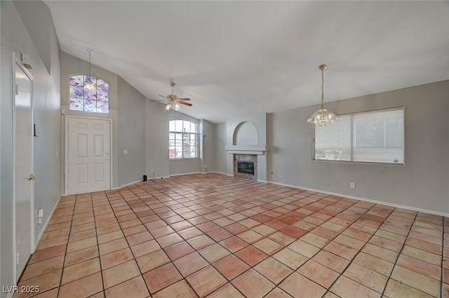 unfurnished living room featuring light tile patterned flooring, vaulted ceiling, ceiling fan with notable chandelier, and a fireplace