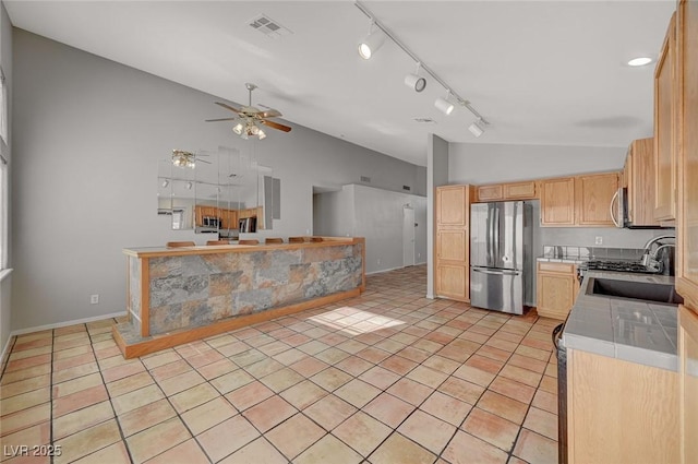 kitchen with light tile patterned flooring, lofted ceiling, sink, stainless steel appliances, and light brown cabinets