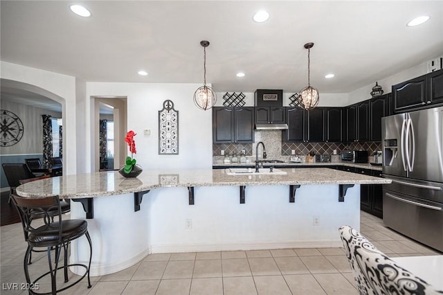 kitchen with a large island, hanging light fixtures, stainless steel fridge, and sink