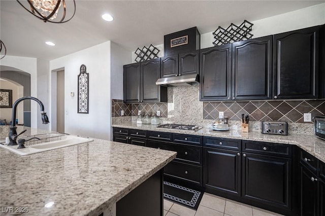 kitchen featuring sink, backsplash, stainless steel gas cooktop, light tile patterned floors, and light stone countertops