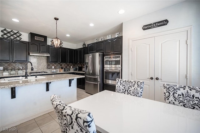 kitchen with a breakfast bar, sink, hanging light fixtures, light tile patterned floors, and stainless steel appliances