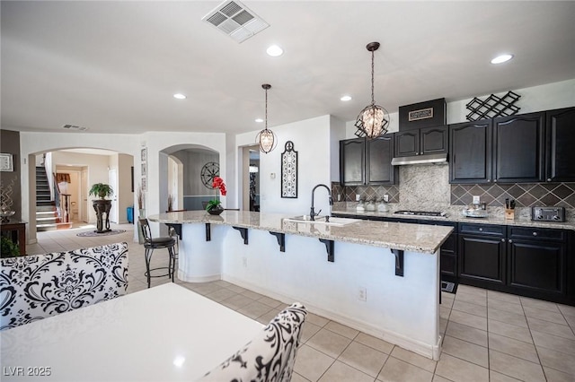 kitchen featuring sink, a center island with sink, tasteful backsplash, a kitchen bar, and decorative light fixtures