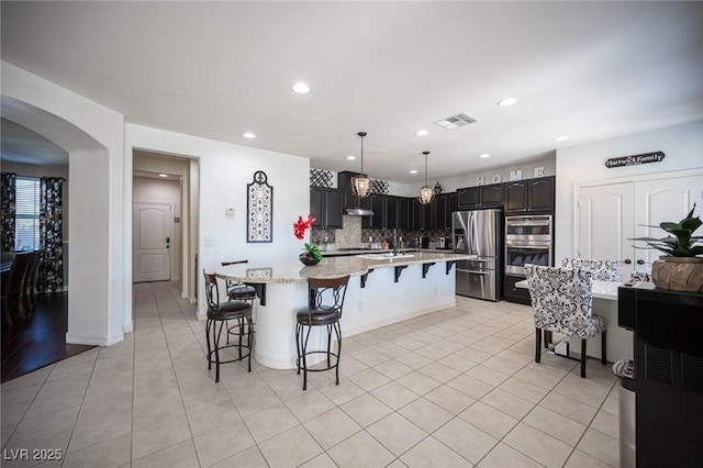 kitchen with tasteful backsplash, appliances with stainless steel finishes, a kitchen bar, and light tile patterned floors