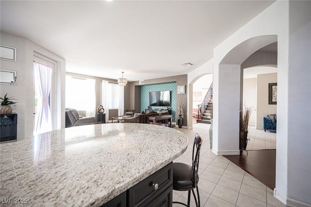 kitchen featuring light tile patterned floors, light stone counters, a kitchen bar, and decorative light fixtures