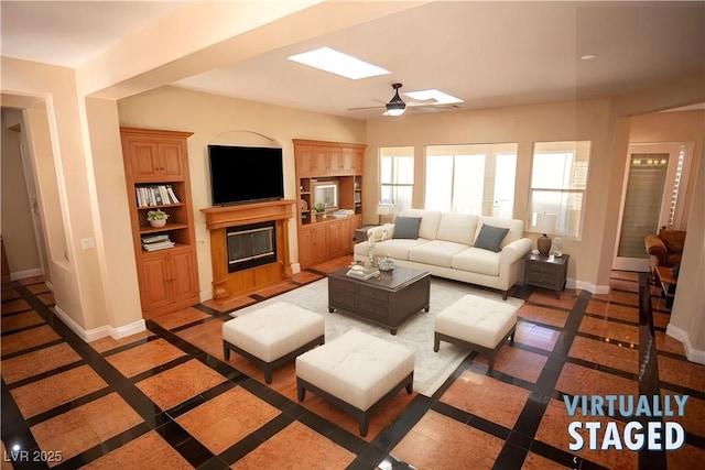 living room with built in shelves, ceiling fan, and a skylight