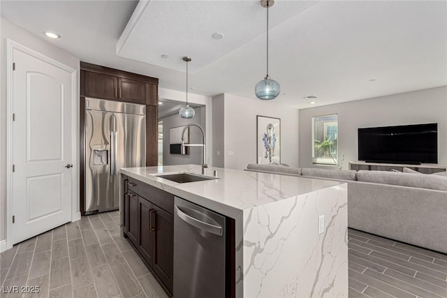 kitchen with sink, light stone counters, hanging light fixtures, a center island with sink, and appliances with stainless steel finishes