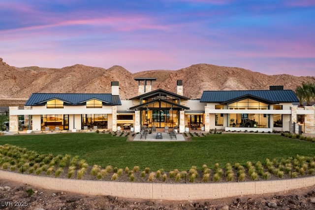 back house at dusk with a patio, a mountain view, and a yard