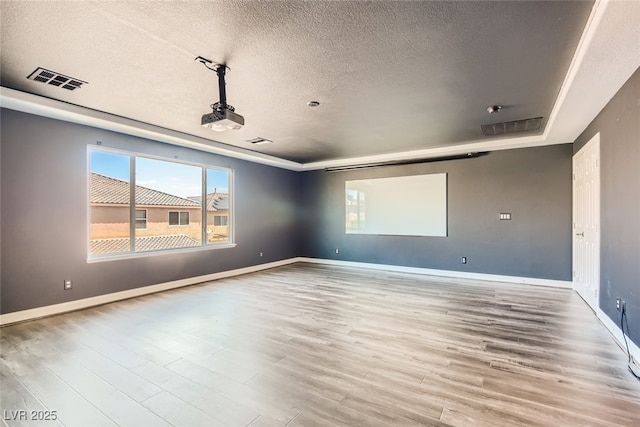 empty room featuring a textured ceiling, light wood-type flooring, and a tray ceiling