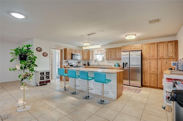 kitchen featuring appliances with stainless steel finishes, a kitchen bar, hanging light fixtures, a center island, and light tile patterned floors