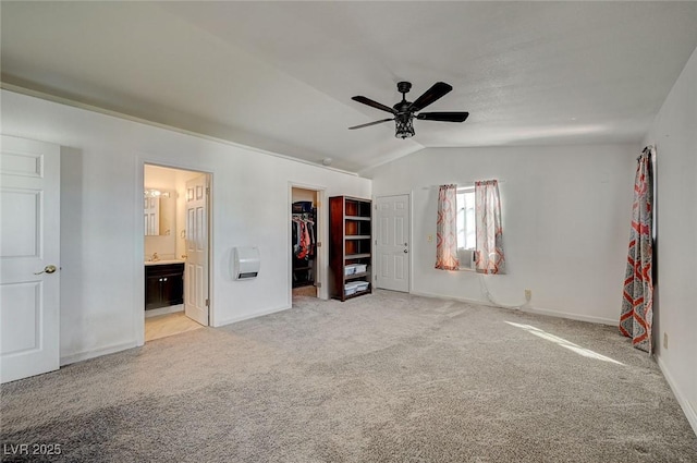 unfurnished bedroom featuring connected bathroom, a walk in closet, vaulted ceiling, light carpet, and ceiling fan