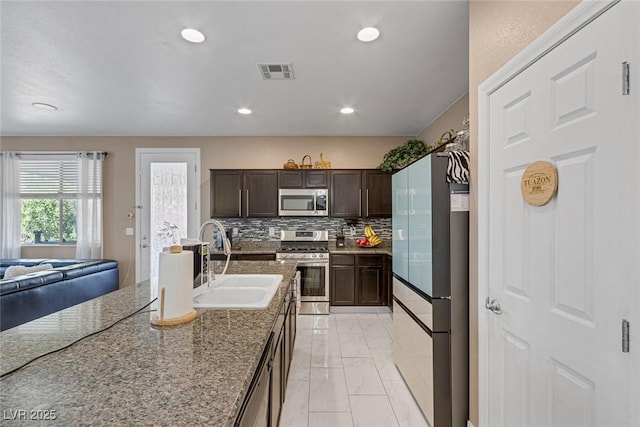 kitchen with sink, tasteful backsplash, dark brown cabinets, stone counters, and stainless steel appliances