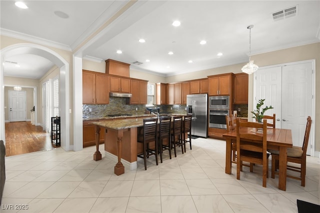 kitchen with pendant lighting, a breakfast bar, appliances with stainless steel finishes, a center island, and light stone counters