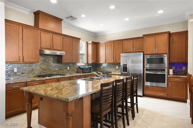 kitchen with sink, a kitchen island with sink, stainless steel appliances, a kitchen breakfast bar, and light stone counters