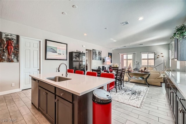 kitchen with a kitchen island with sink, sink, dark brown cabinetry, and dishwasher