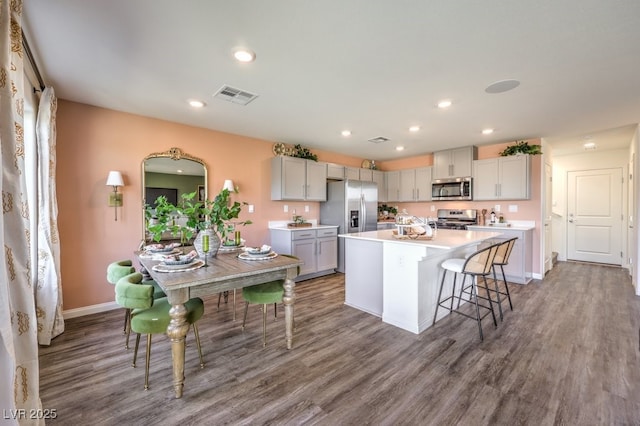 kitchen featuring stainless steel appliances, wood-type flooring, gray cabinets, and a center island with sink