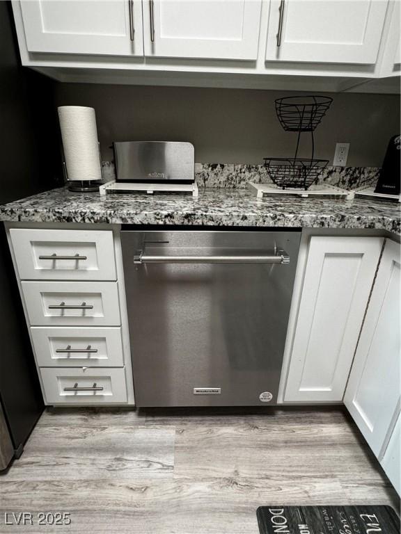 kitchen featuring white cabinets, light hardwood / wood-style floors, dark stone counters, and dishwasher