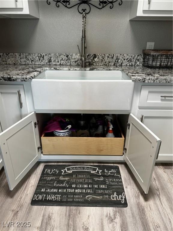 room details featuring white cabinetry, sink, light stone counters, and light wood-type flooring